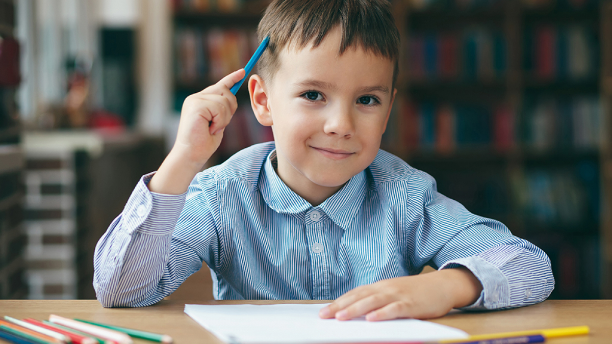 Cute  smiling boy doing homework,  coloring pages, writing and painting . Children paint. Kids draw. Preschooler with books in the library. Colorful pencils and paper on a desk. Creative boy.