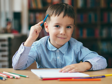 Cute  smiling boy doing homework,  coloring pages, writing and painting . Children paint. Kids draw. Preschooler with books in the library. Colorful pencils and paper on a desk. Creative boy.