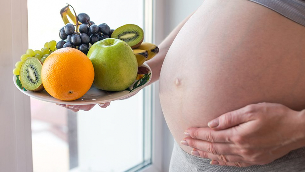 A pregnant woman with belly holding a plate with fruits in hand. The concept for weight control and healthy eating during pregnancy
