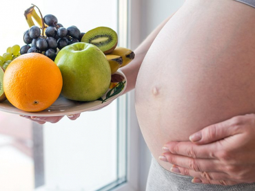 A pregnant woman with belly holding a plate with fruits in hand. The concept for weight control and healthy eating during pregnancy